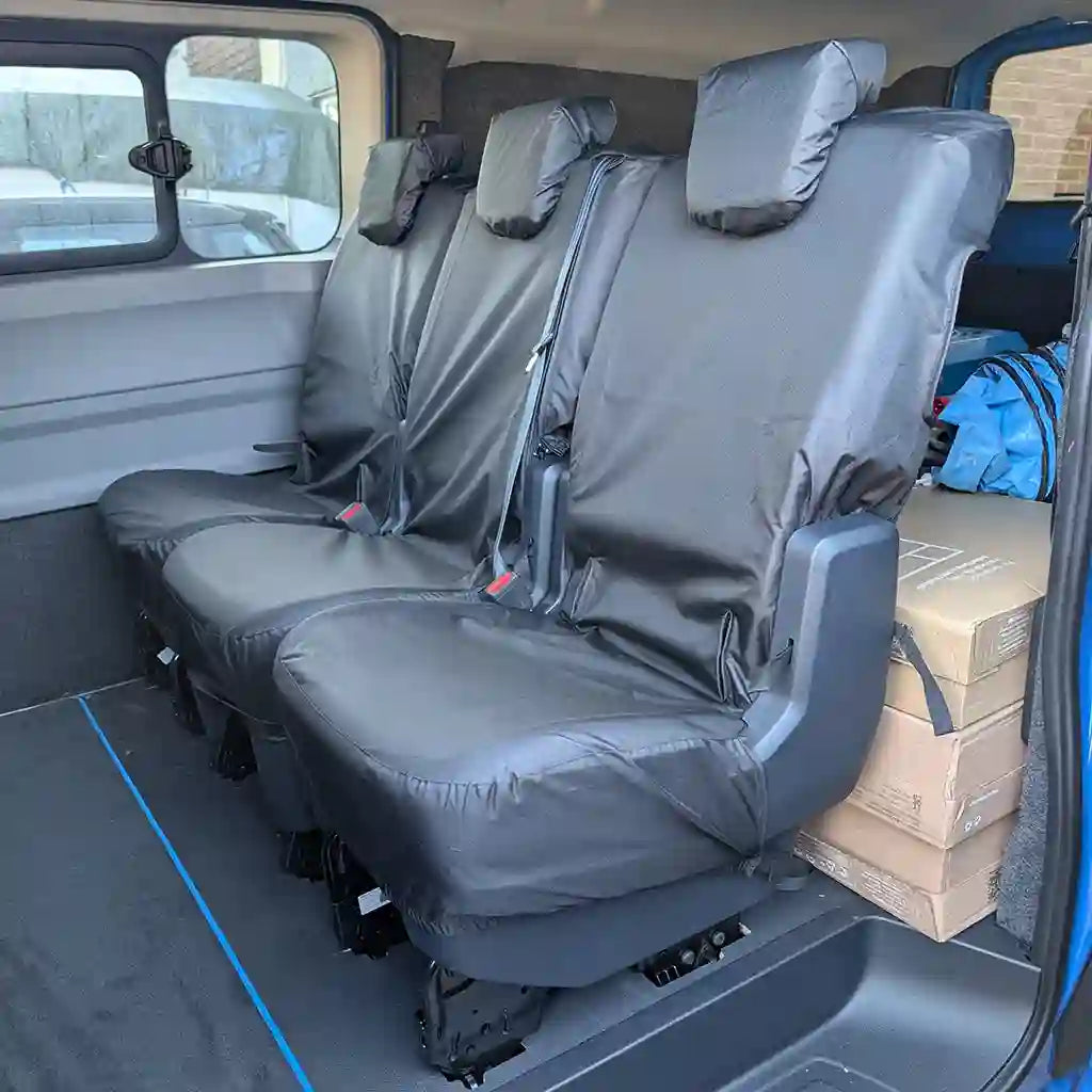 Black vehicle seat covers on seats of a VW T7 KOMBI van with boxes in the cargo area.