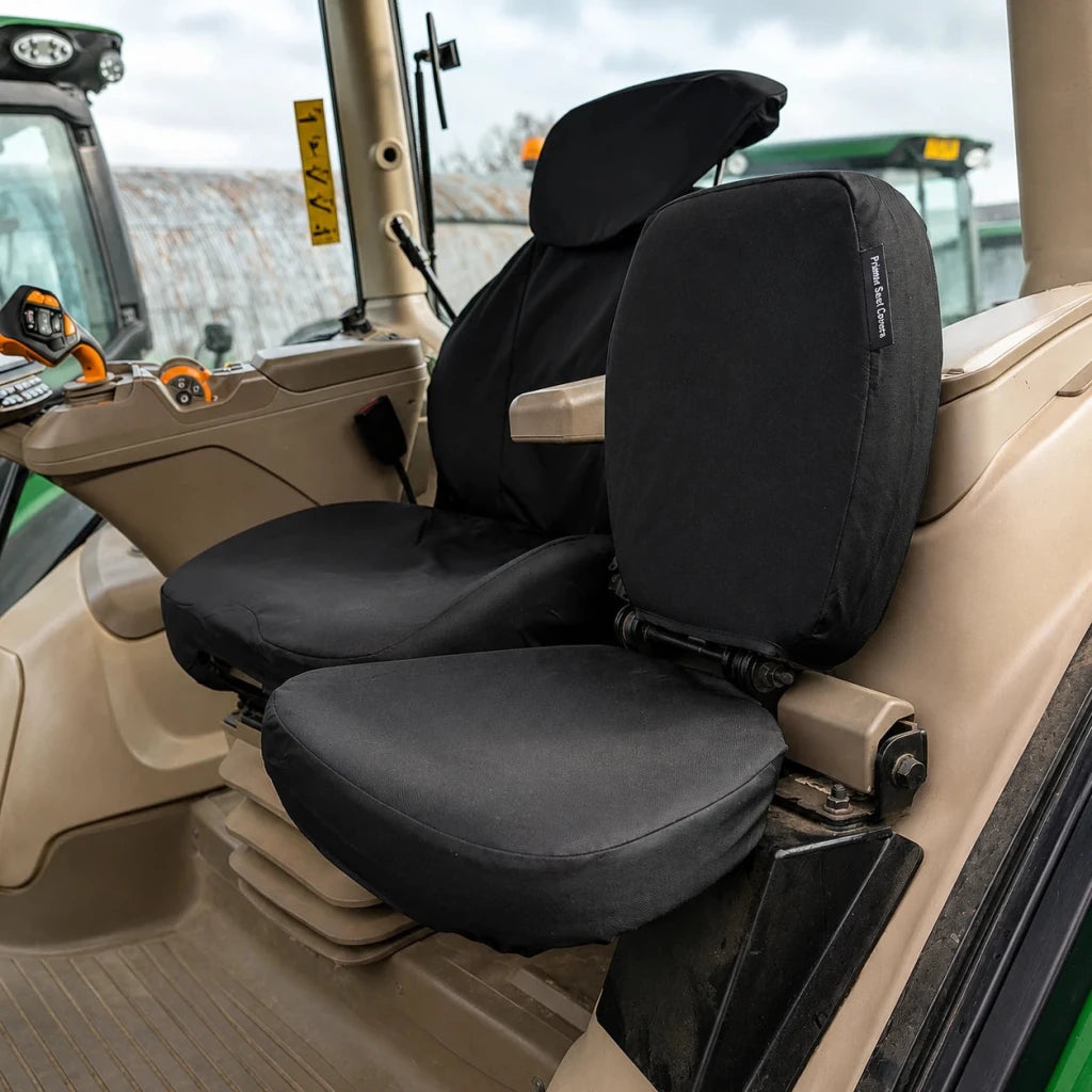 Black seat covers installed on a tractor cabin seat, shown in a real vehicle interior with beige upholstery and visible tractor cabin details.