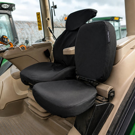 Black seat covers installed on a tractor cabin seat, shown in a real vehicle interior with beige upholstery and visible tractor cabin details.